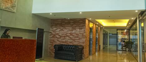 A lobby with a reception desk, a black leather sofa, a brick wall, and glass doors leading to another area.