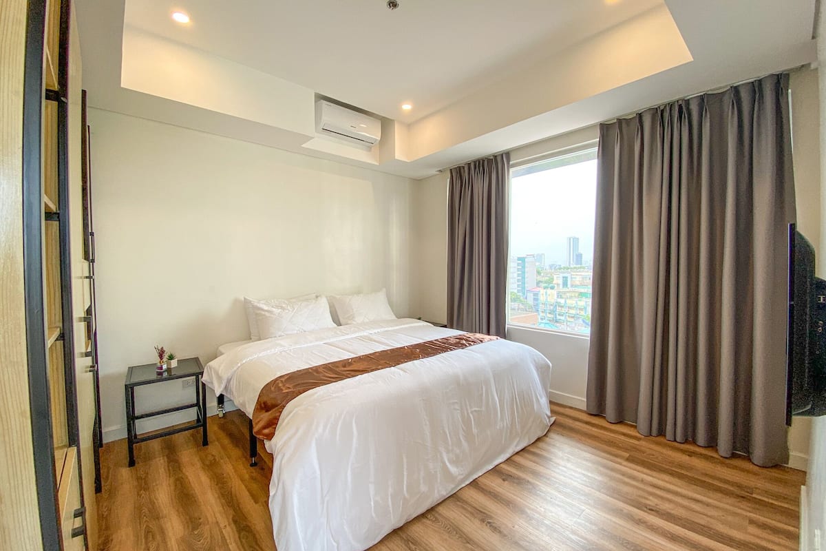A hotel room with a large bed, a small bedside table, a window with curtains, and a city view.