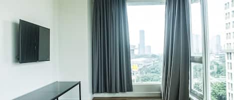 A modern hotel room with a large window, a flat-screen TV mounted on the wall, and a wooden floor.