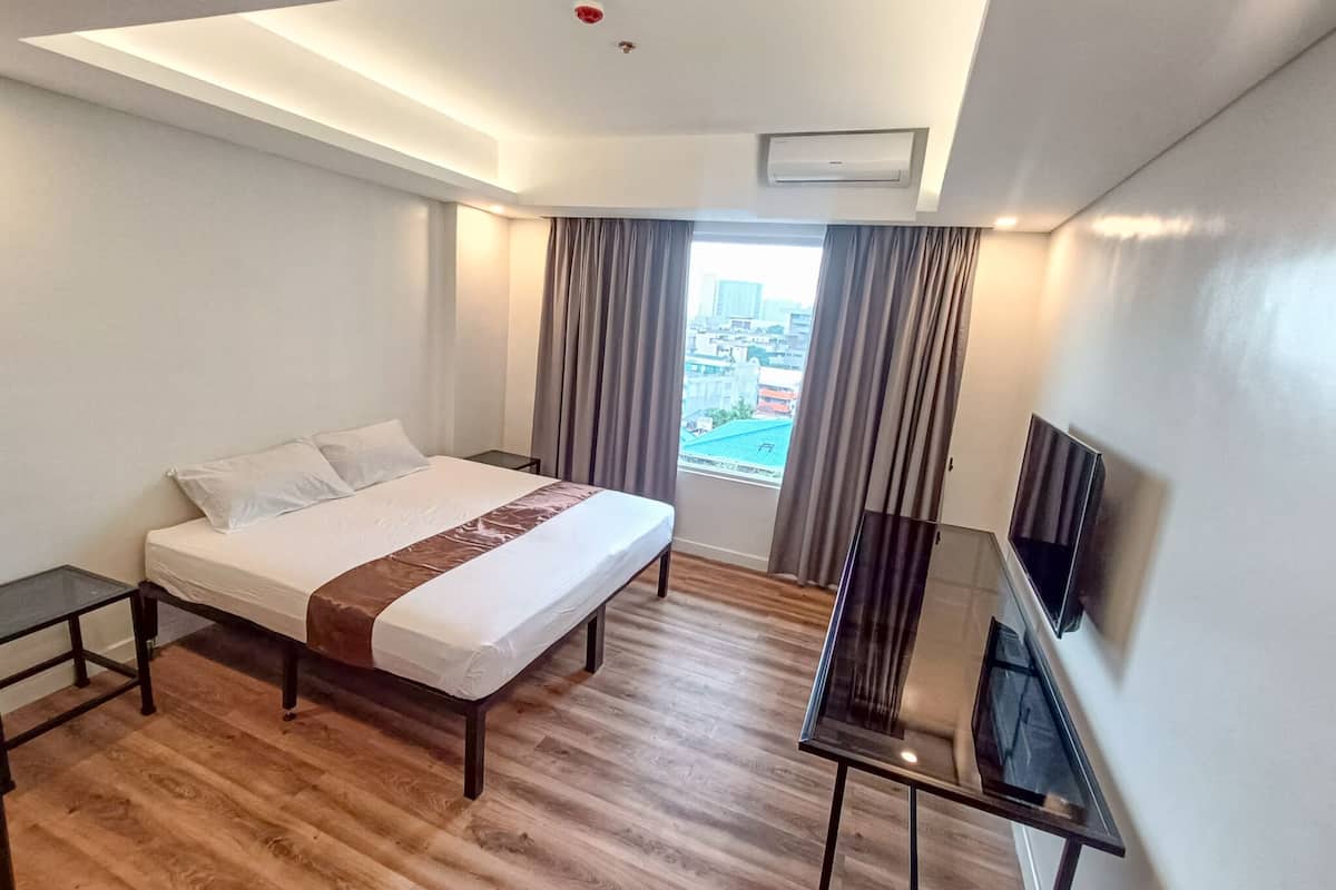 A hotel room with a bed, a TV, a desk, and a window with curtains.