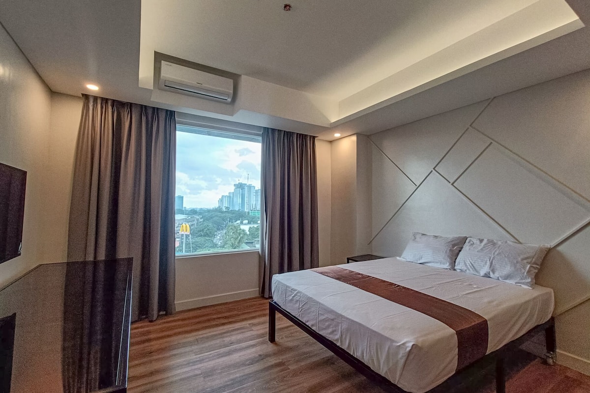 A modern hotel room with a large bed, a view of the city, and an air conditioning unit on the wall.