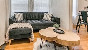 A living room with a dark grey sofa, two round wooden tables, and a white knitted throw blanket.