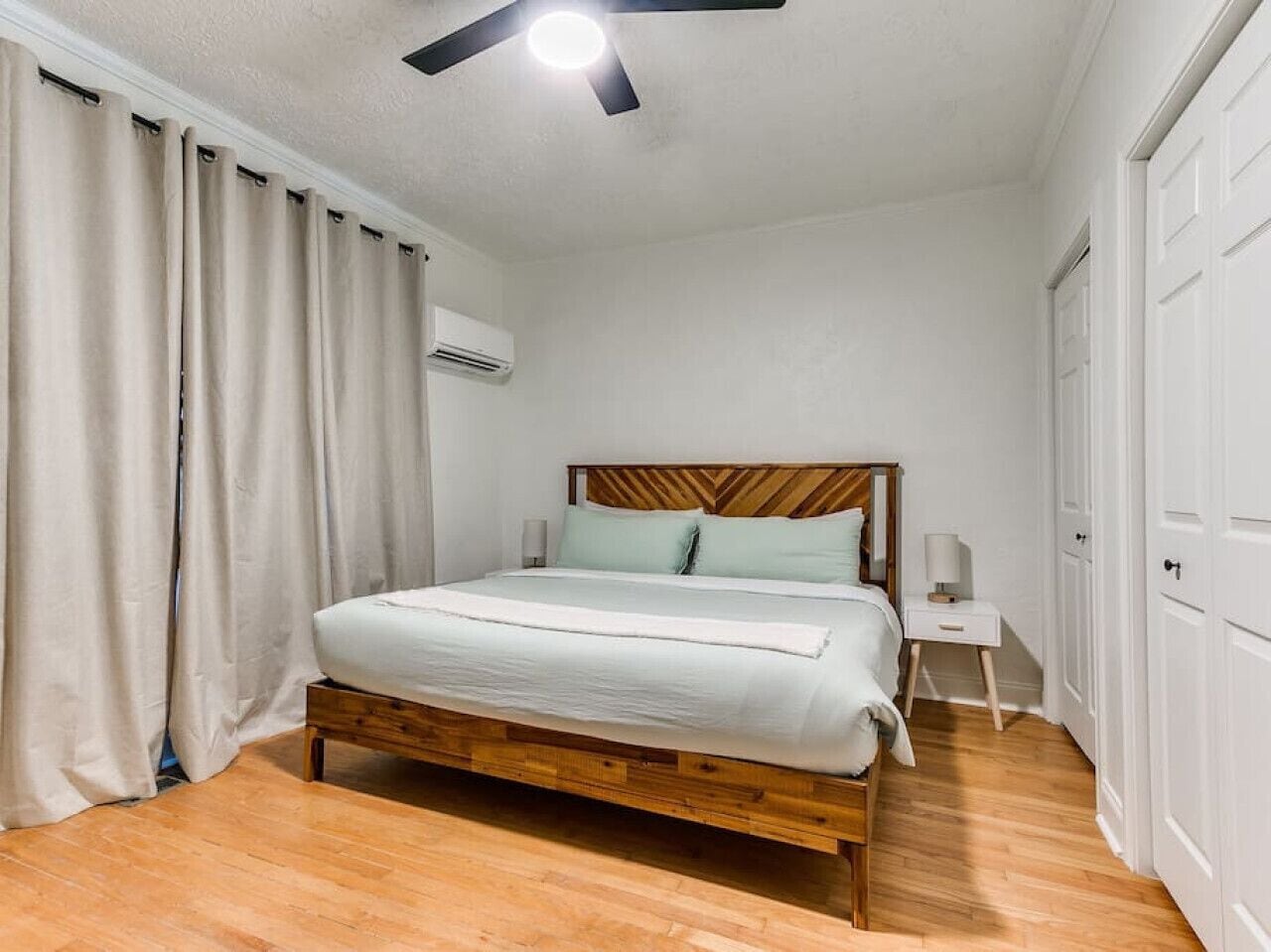 Una camera da letto con un letto di legno, biancheria bianca, un comodino, una ventola a soffitto e un armadio.