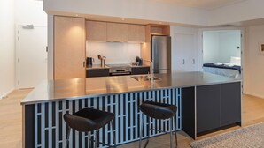 Uma cozinha moderna com ilha central, dois bancos altos e forno embutido.