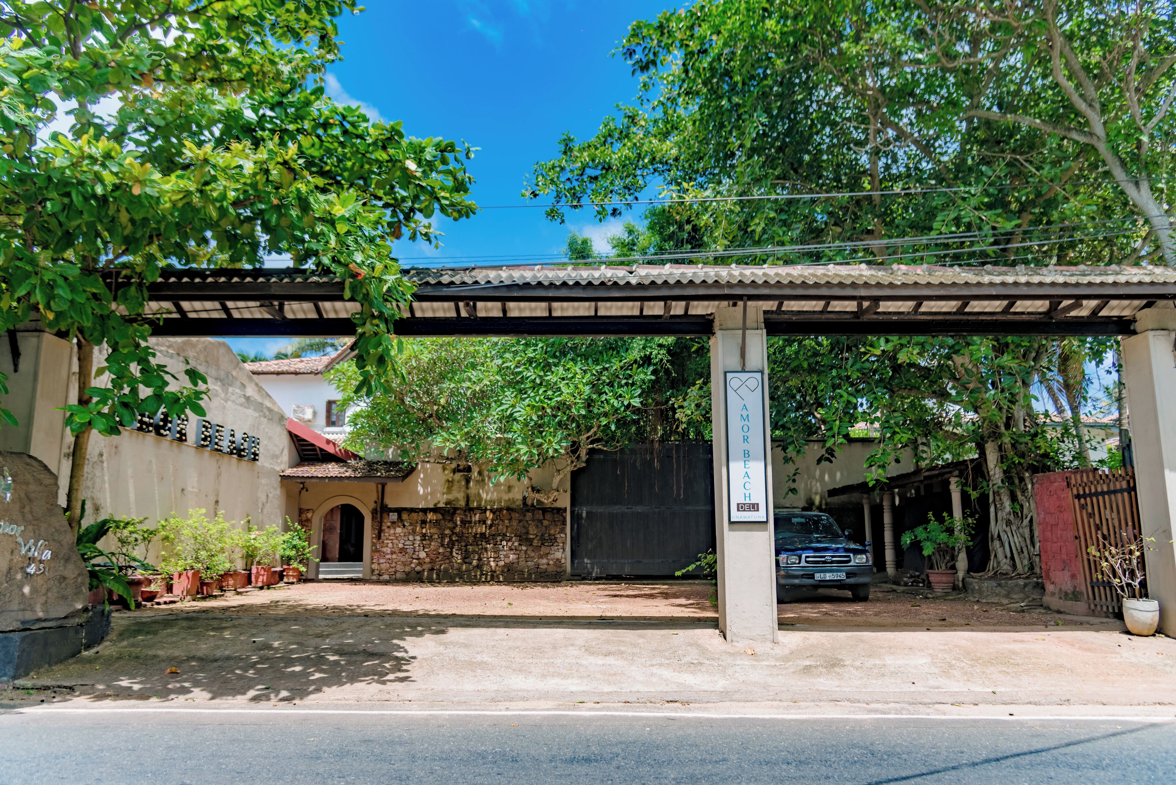 A covered parking area with a car, potted plants, and a stone wall.