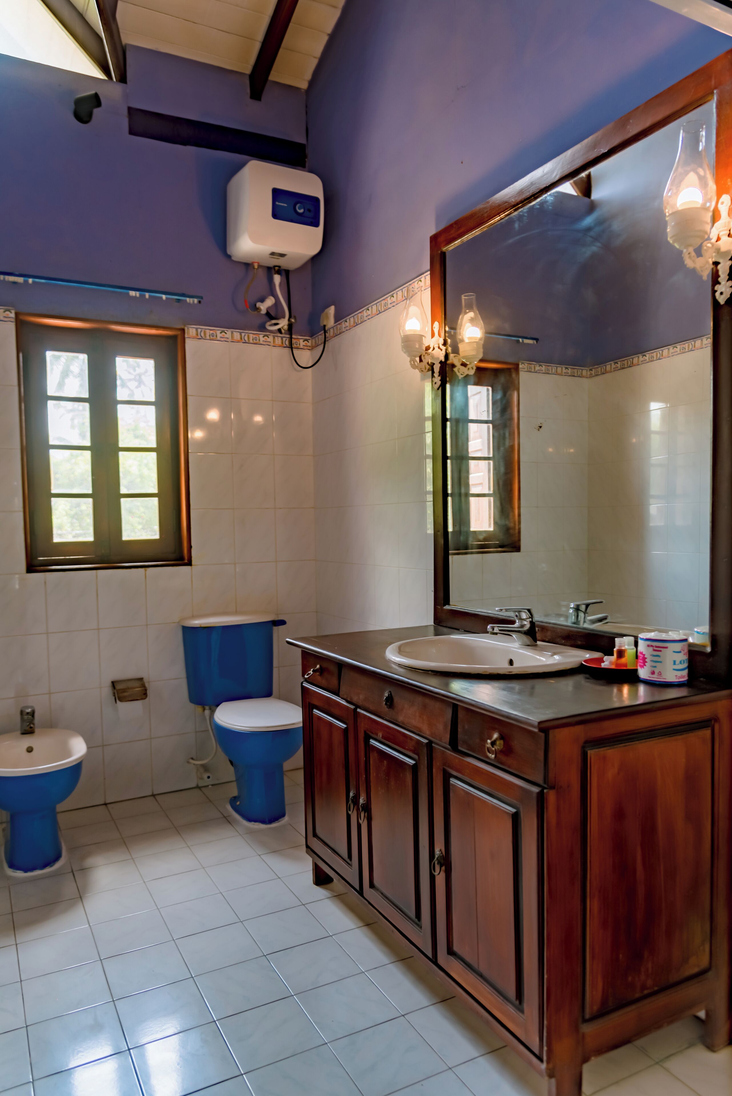 Ein Badezimmer mit einem Holzbadschrank, einem großen Spiegel und zwei blauen Toiletten.