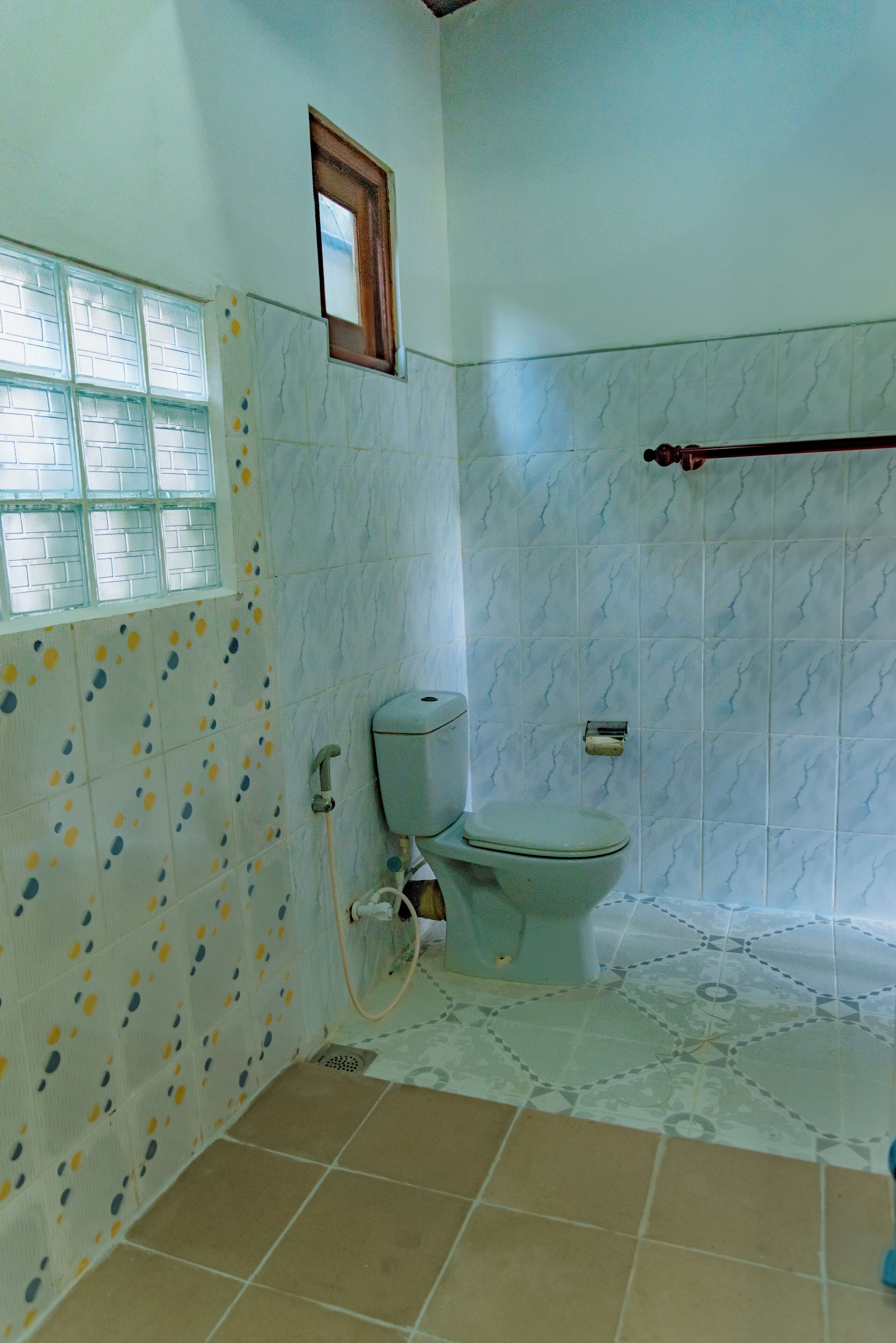 A bathroom with a toilet, a small window, and patterned tiles on the walls and floor.