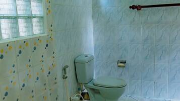 A bathroom with a toilet, a small window, and patterned tiles on the walls and floor.