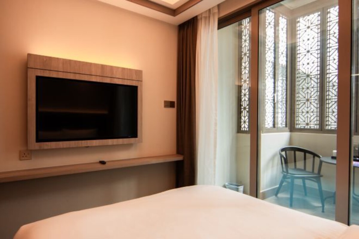 Une chambre d’hôtel avec un lit, un téléviseur fixé au mur, une fenêtre donnant sur un balcon et une chaise à l’extérieur.