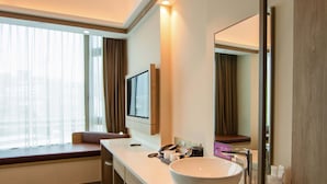 Une salle de bain moderne avec un grand lavabo blanc, un miroir et une fenêtre avec des rideaux.