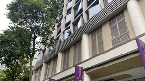 Un hôtel moderne à la façade imposante, doté de grandes fenêtres et d’une enseigne indiquant qu’il s’agit de l’hôtel Aqueen Prestige.