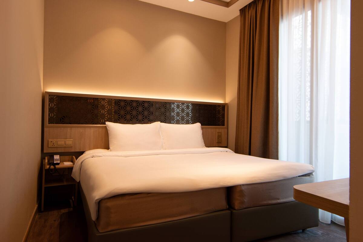 Ein Hotelzimmer mit einem großen Bett, einem Nachttisch und einem Fenster mit Vorhängen.