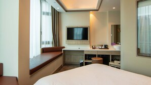 Une chambre d’hôtel moderne dotée d’un grand lit, d’un téléviseur à écran plat fixé au mur, d’un bureau avec un ordinateur et un téléphone, d’un coin salon avec un banc rembourré et d’une petite poubelle.