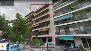 A multi-story residential building with balconies, a gated parking area, and a street view.