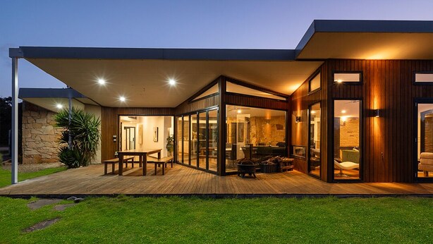 Ein modernes Haus mit einer überdachten Terrasse, Glasüren und einer Steinsäule.
