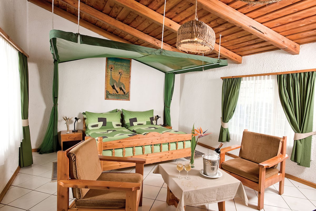 A room with a bed, wooden furniture, a table with drinks, and a painting on the wall.