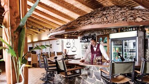 Una zona de bar rústica con pared de piedra, techo de madera y un barman.