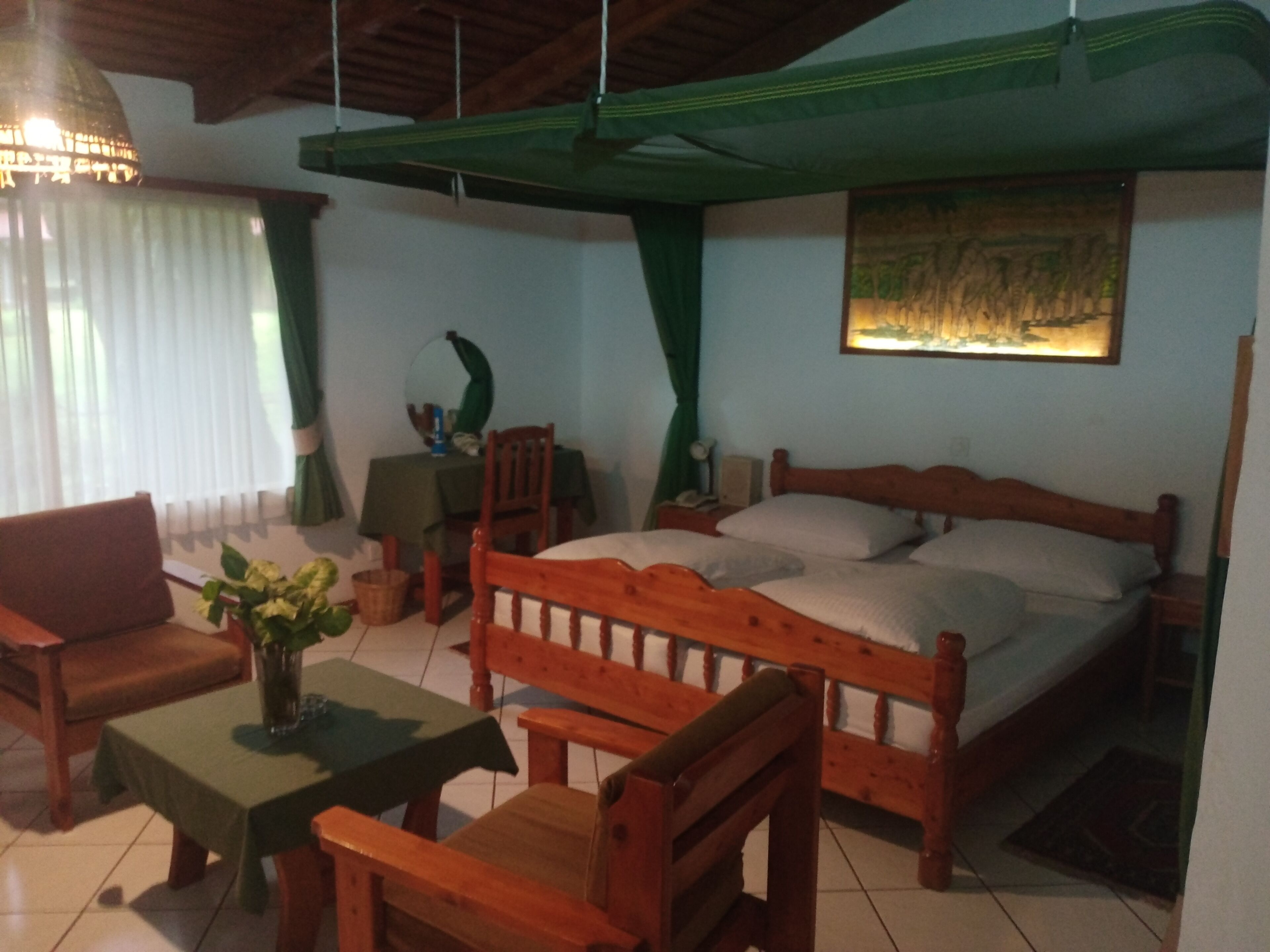 Una habitación con una cama, una silla de madera, una mesita pequeña y una lámpara colgante.