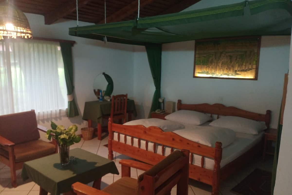 A room with a bed, a wooden chair, a small table, and a hanging lamp.