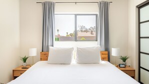 A hotel room with a large bed, two bedside tables with lamps, a window with curtains, and a view of the outside.