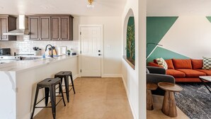 A modern kitchen with a white island, dark wooden stools, and a green accent wall.