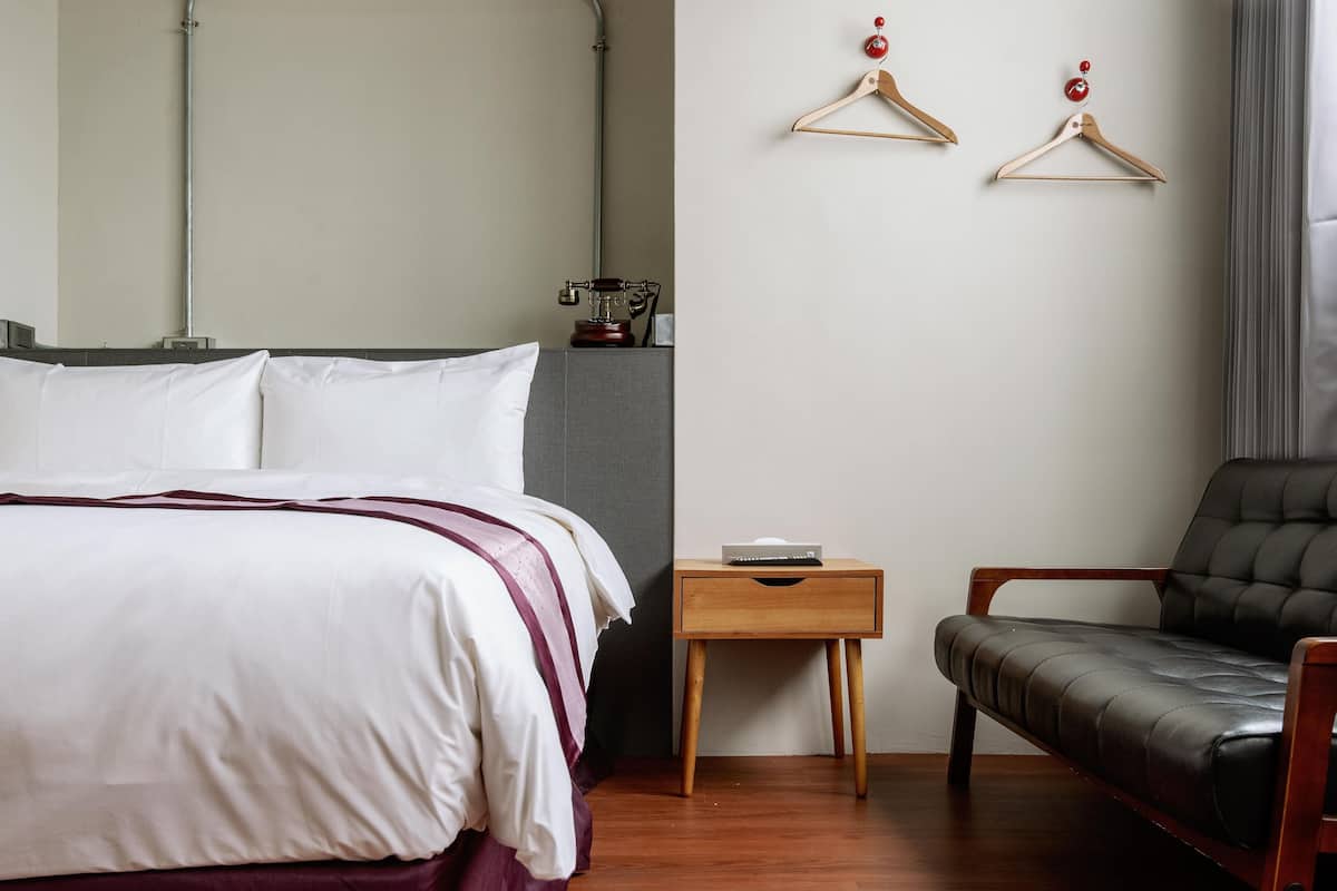 A hotel room with a bed, a wooden nightstand, a black leather chair, and two wooden hangers on the wall.