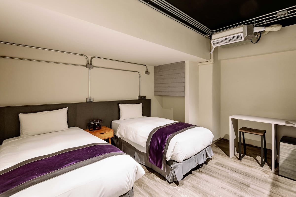 A hotel room with two beds, a desk, and a chair.