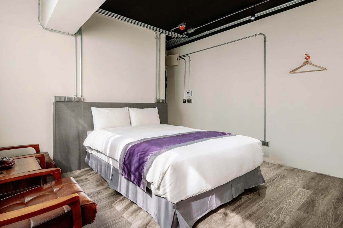 A modern hotel room with a neatly made bed, a wooden bench, and a hanging coat rack.