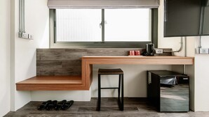 A compact room with a built-in desk, a small stool, a black refrigerator, and a window with blinds. - SATURN HOTEL (Taichung)