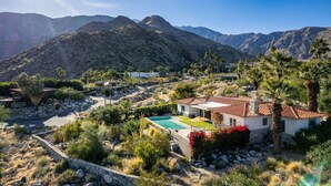 A villa with a swimming pool, surrounded by mountains and palm trees.