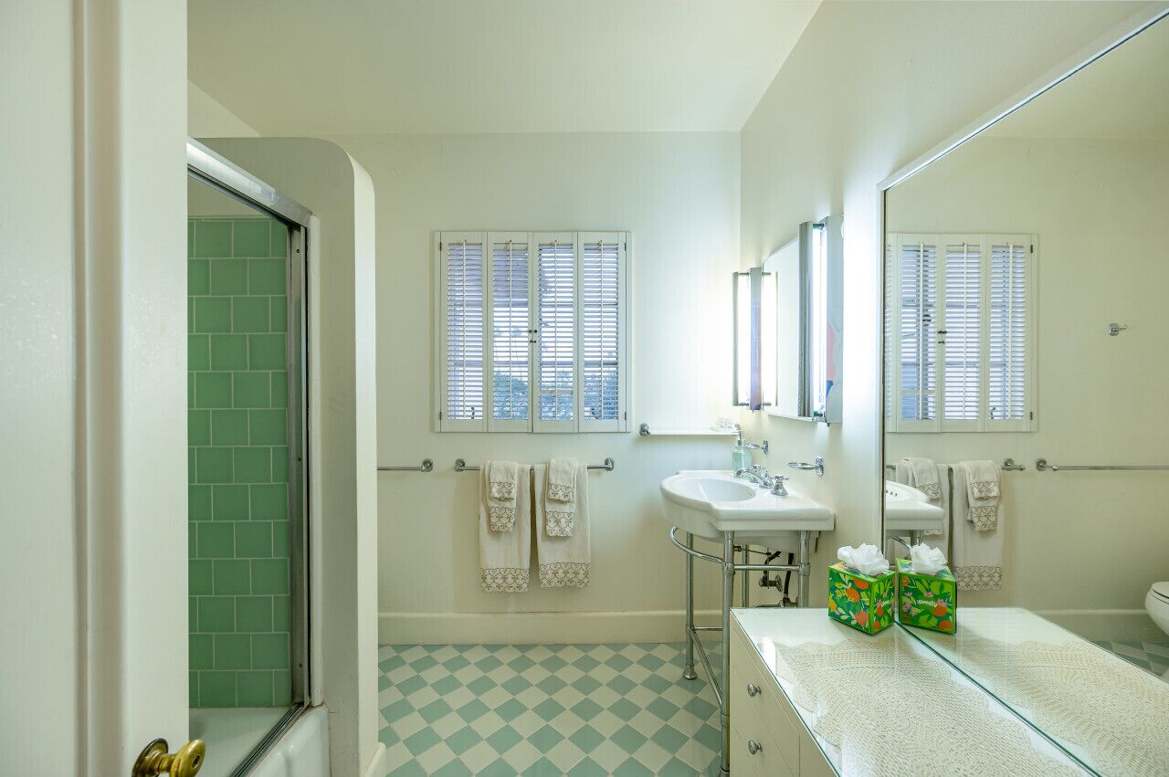 Un baño con lavamanos, espejo y persianas.