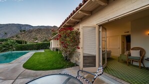 A house with a swimming pool, a patio with a glass table and chairs, and a view of mountains.