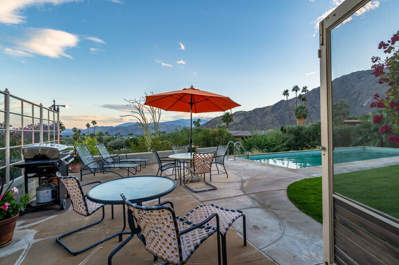 An outdoor patio with a pool, chairs, and a grill.