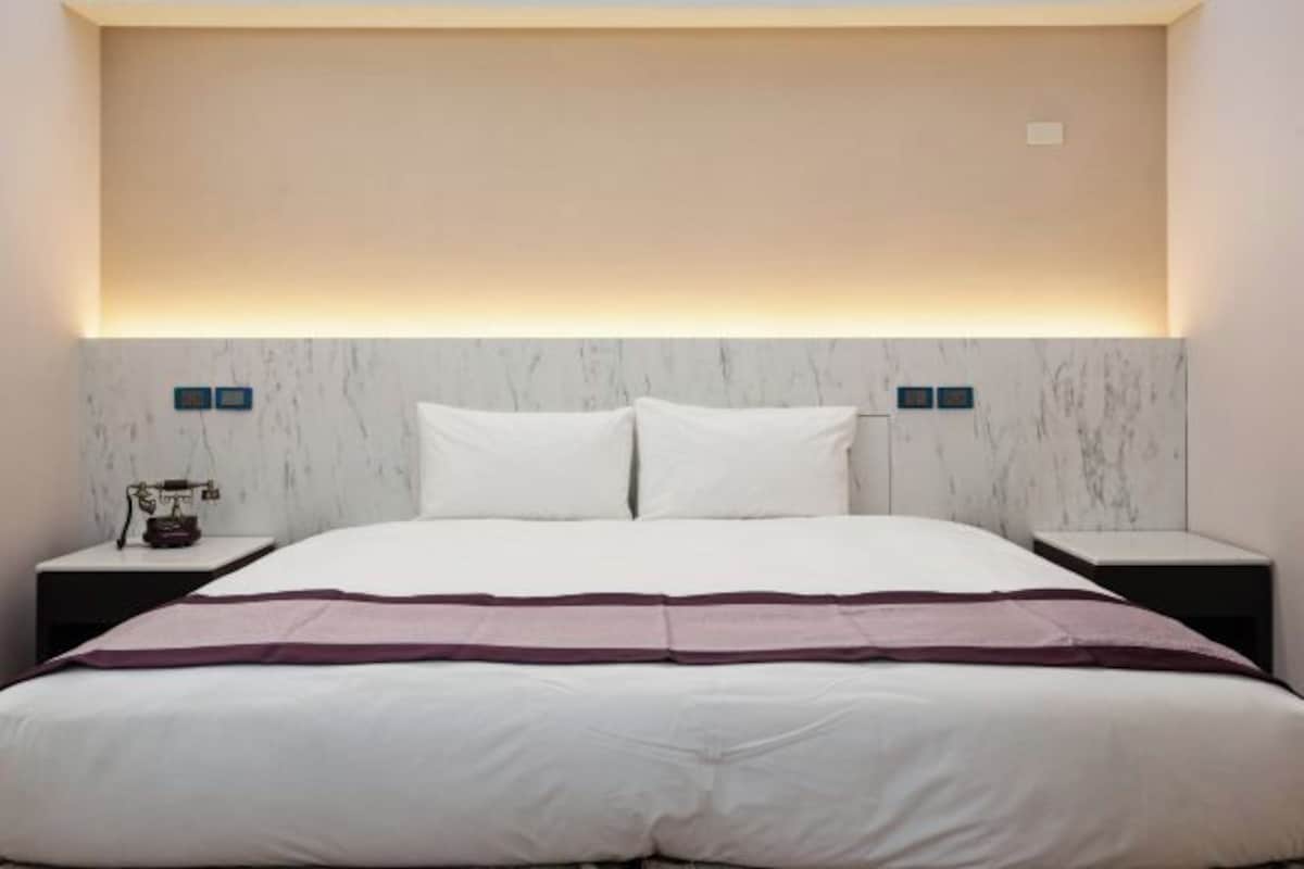 A modern hotel room with a large bed, marble headboard, and bedside tables with lamps.