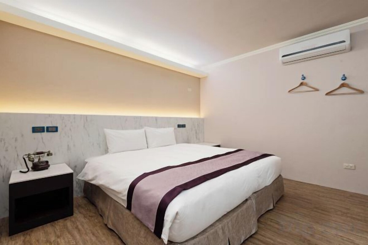 A hotel room with a bed, bedside table, and a wall-mounted air conditioner.
