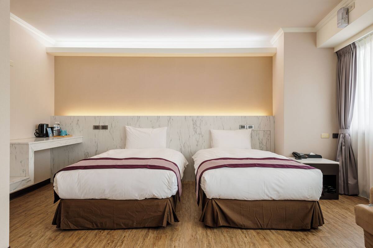 A hotel room with two beds, a desk, and a nightstand.