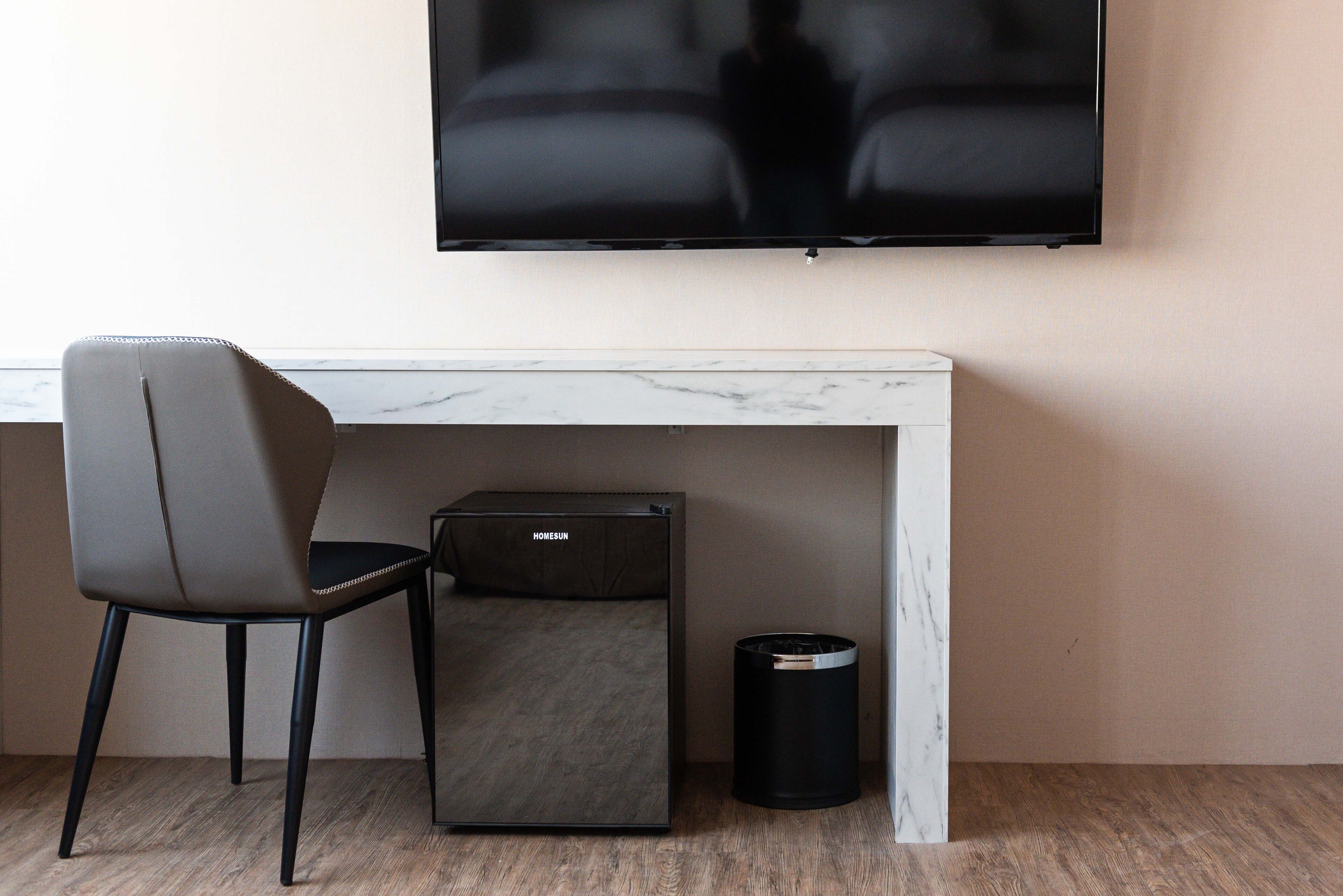 Una habitación moderna con un escritorio de mármol, una silla negra, un televisor y un cesto de basura.