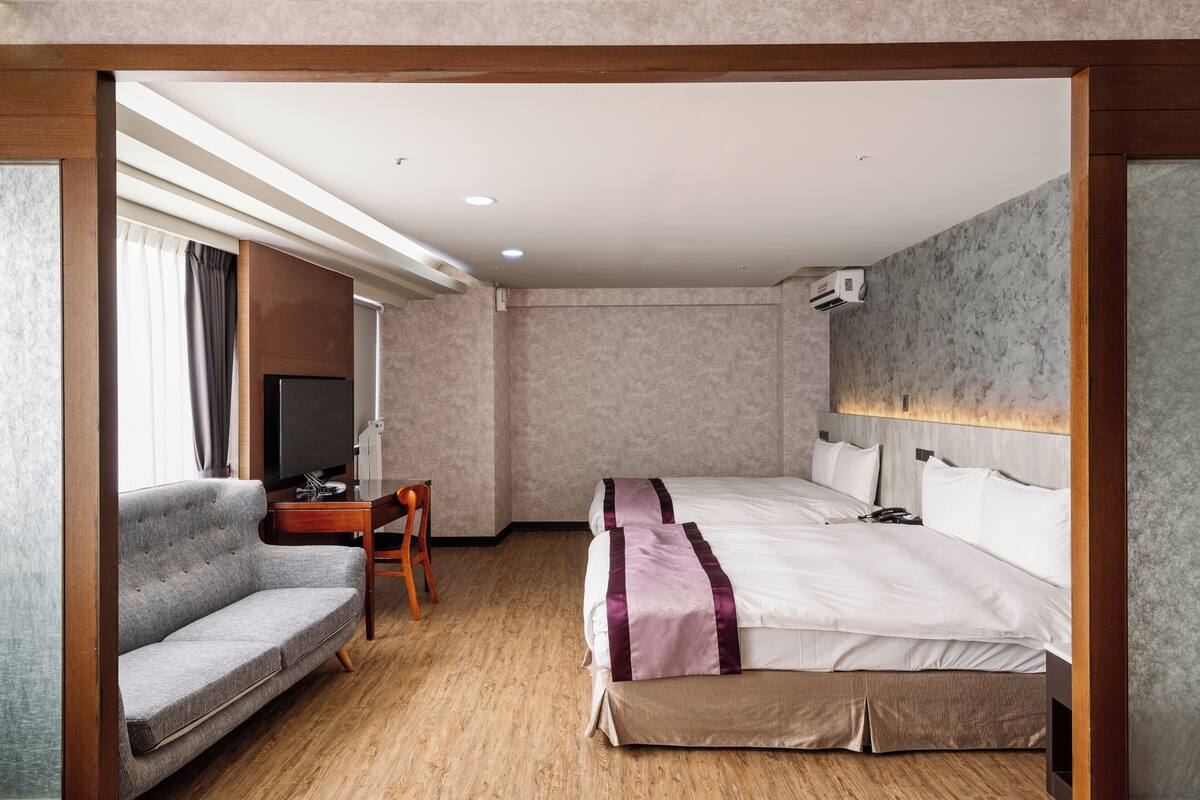 A hotel room with a bed, a sofa, a desk, and a television.