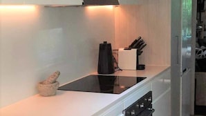 Ett modernt kök med vita skåp, en svart induktionshäll, en inbyggd ugn och ett knivblock.