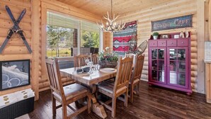 A wooden cabin interior with a dining table, chairs, a chandelier, a cabinet, and a sign reading "Cowboy Cafe".