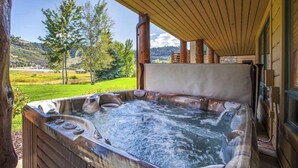 A hot tub with a wooden deck and a view of a green landscape.