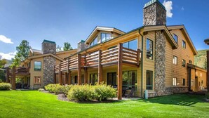 A modern log cabin with a stone chimney, wooden deck, and a well-maintained lawn.