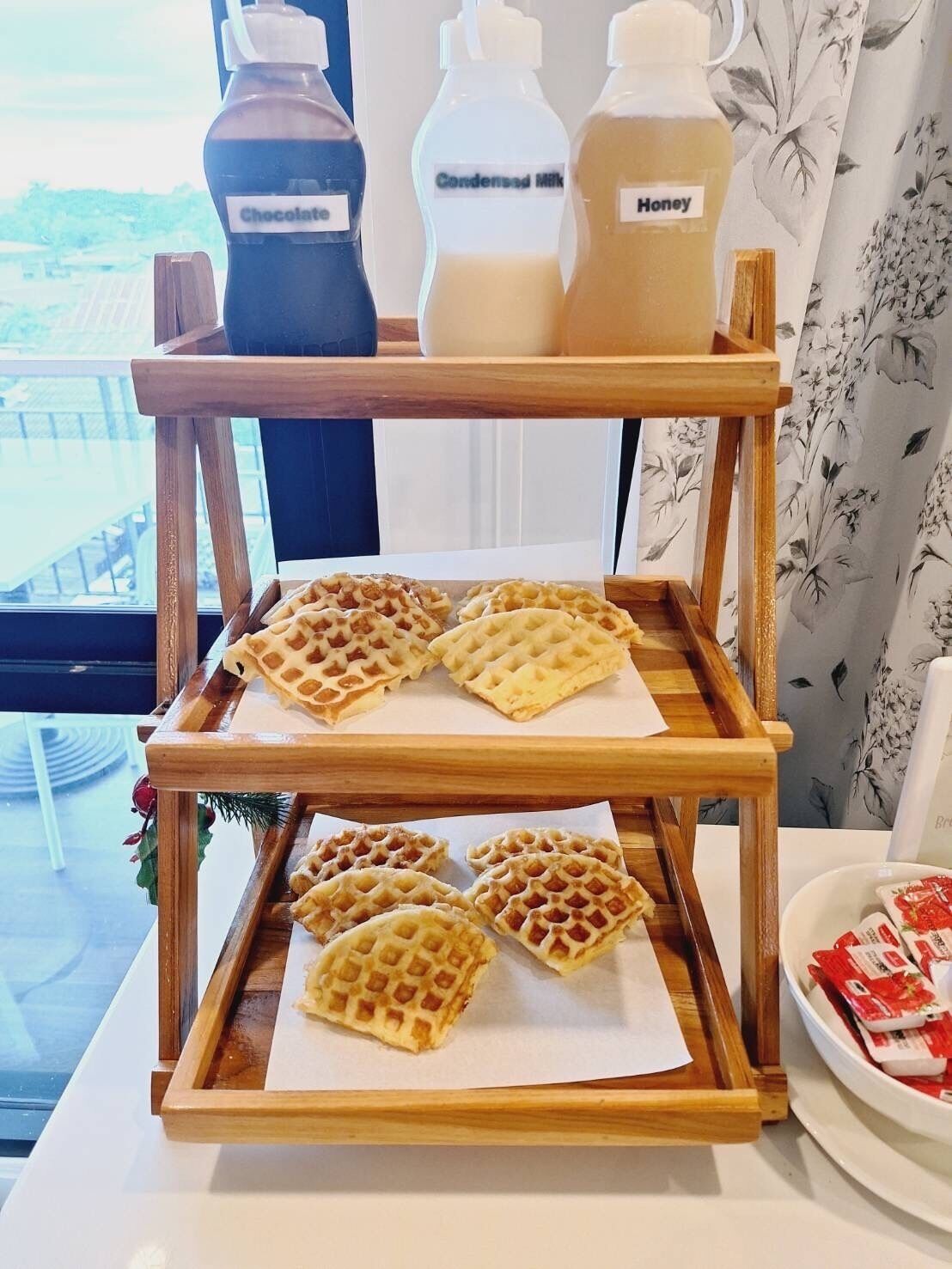 A wooden serving tray with waffles and condensing milk, honey, and chocolate syrup bottles.