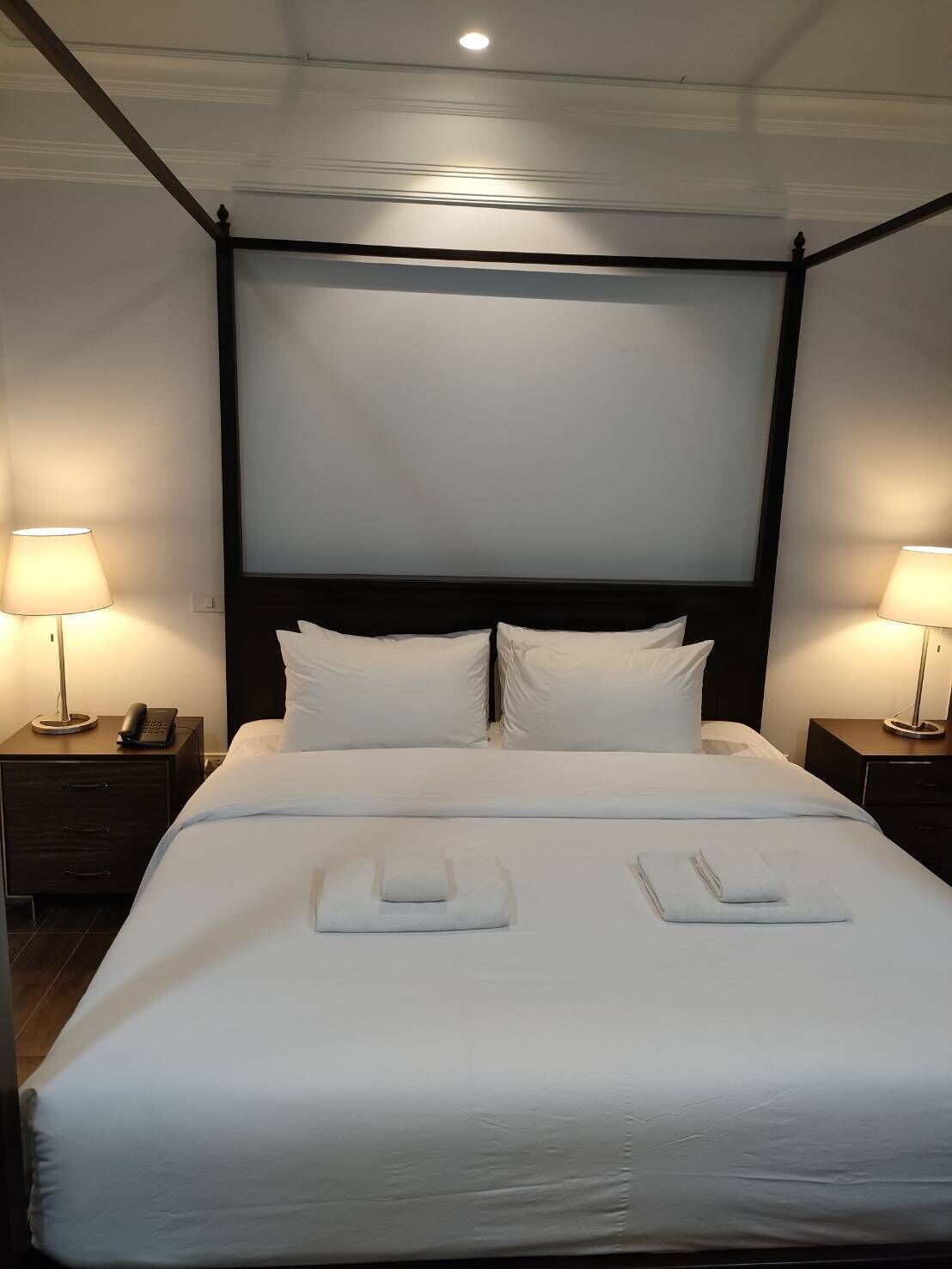 A neatly made bed with white linens and pillows, two bedside tables with lamps, and a dark headboard.