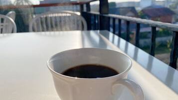 Una taza de café blanco sobre una mesa de balcón con vistas a edificios y una palmera.