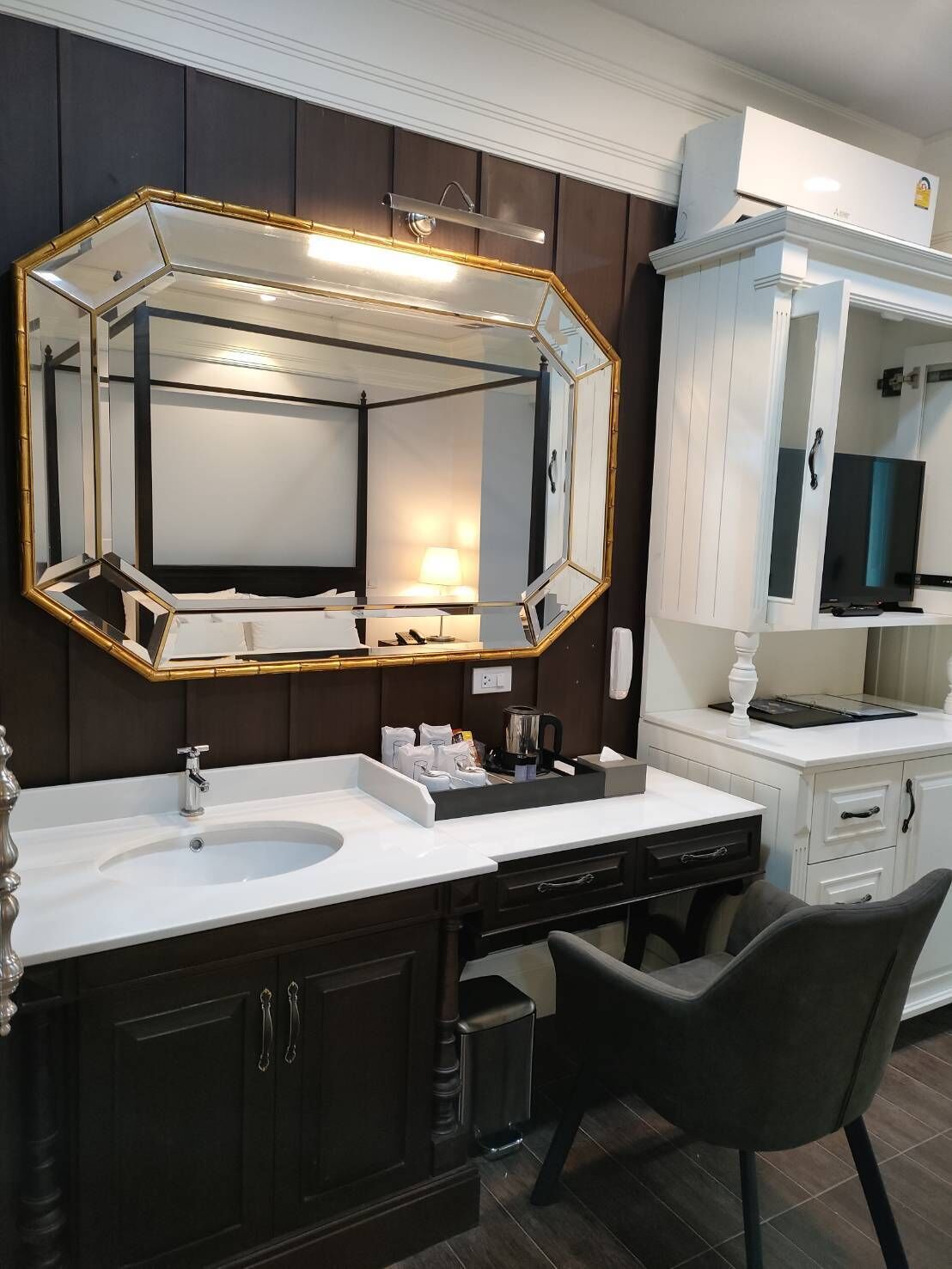 A modern bathroom with a large mirror, dark wood cabinets, a white vanity, and a black chair.