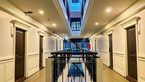 Un pasillo de hotel con una escalera central, puertas dobles a ambos lados y un tragaluz en el techo.