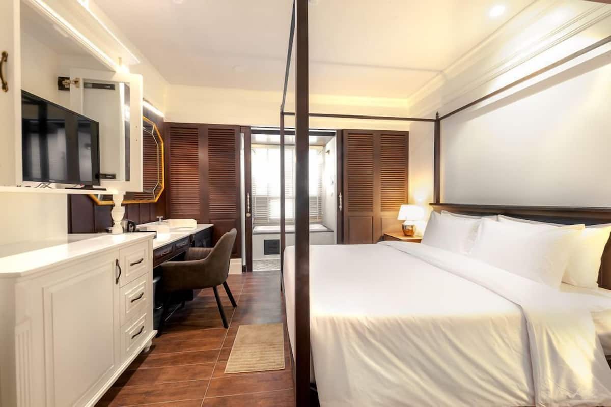 Ein Hotelzimmer mit einem großen Bett, einem Schreibtisch mit Stuhl, einem Fernseher und einem Fenster mit Jalousien.