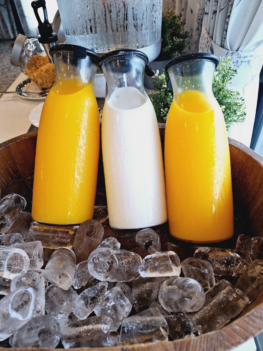 Eine Holzschüssel gefüllt mit Eiswürfeln und drei Glasflaschen mit Orangensaft und Milch.