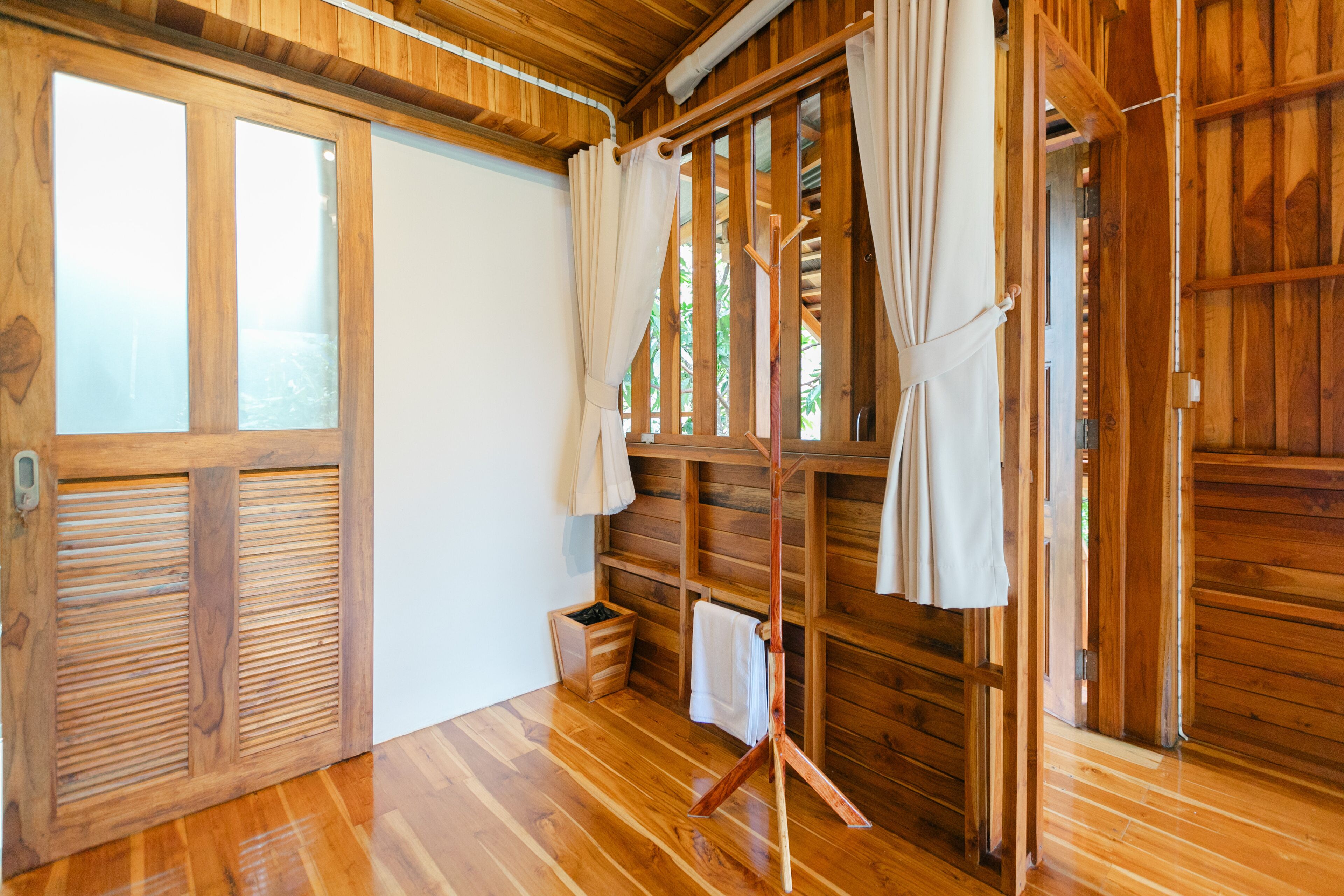 A wooden room with a sliding door, a wooden bench, and a curtain rod.